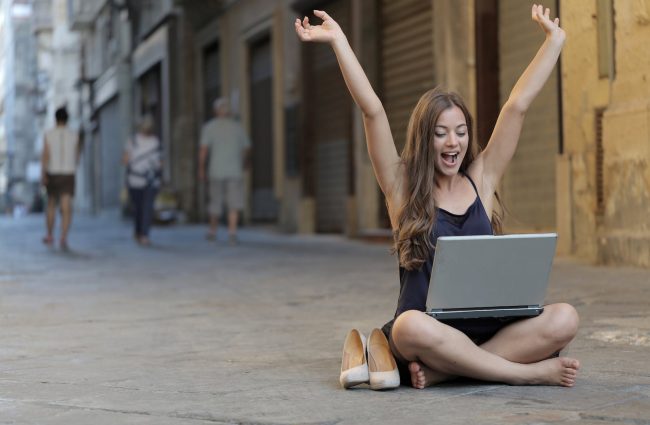 Was ist ein Digitaler Nomade? - woman raising her hands up while sitting on floor with macbook pro on lap