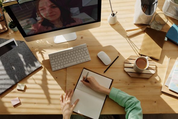 Unternehmenskultur für Remote-Mitarbeiter person in a videocall writing on notebook