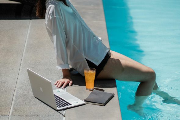 anonymous woman dipping feet in pool water after online work on netbook